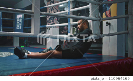 Tired and exhausted African American fighter sits in ring corner Tired and exhausted African American fighter sits in ring corner 110964169