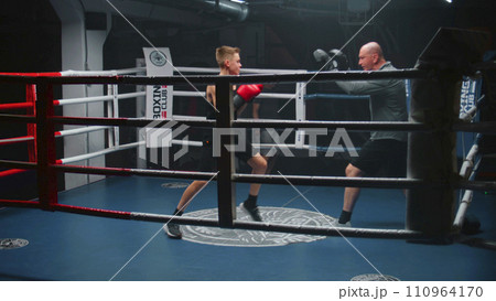 Teenager in boxing gloves trains and exercises with adult trainer Teenager in boxing gloves trains and exercises with adult trainer 110964170