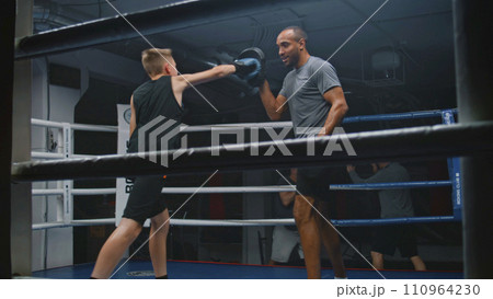 Young boy in boxing gloves hits punching mitts and practices Young boy in boxing gloves hits punching mitts and practices 110964230