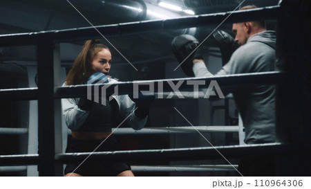 Athletic woman hits punching mitts on boxing ring Athletic woman hits punching mitts on boxing ring 110964306