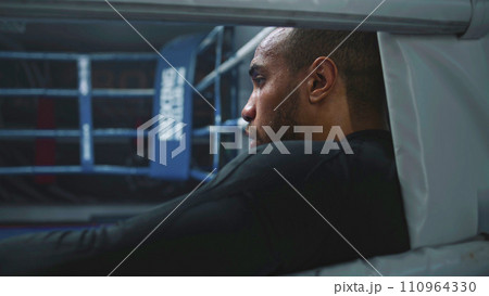 Fighter with beads of sweat on face rests in boxing ring corner Fighter with beads of sweat on face rests in boxing ring corner 110964330