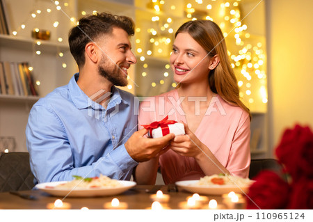 Man presents gift to woman, sharing a joyful moment at dinner Man presents gift to woman, sharing a joyful moment at dinner 110965124