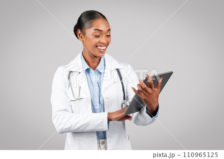 Smiling pretty millennial black woman doctor therapist in white coat typing on tablet, chatting Smiling pretty millennial black woman doctor therapist in white coat typing on tablet, chatting 110965125