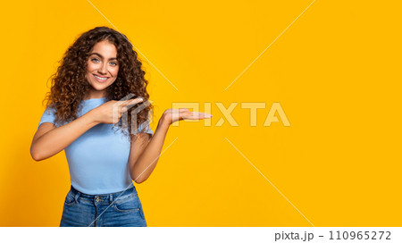Cheerful woman presenting with hand on yellow, free space 110965272