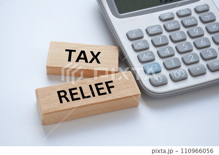 Tax relief text on wooden blocks on white cover background with calculator background. Taxation concept. Tax relief text on wooden blocks on white cover background with calculator background. Taxation concept. 110966056
