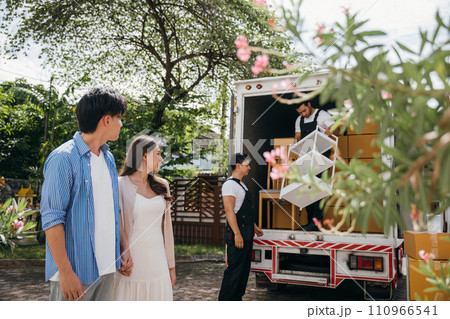 Professional movers assist a smiling newlywed couple captured in a portrait while loading furniture onto a truck. Quality service and teamwork ensure customer satisfaction. Moving Day Concept 110966541