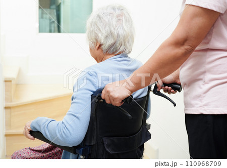 Asian senior woman on wheelchair with caregiver help support walking down the stairs prevent accident, slip and fall at home. Asian senior woman on wheelchair with caregiver help support walking down the stairs prevent accident, slip and fall at home. 110968709