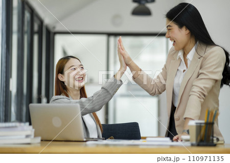 Two women are high-fiving with joy at their success in business. and celebrate performance and teamwork. Two women are high-fiving with joy at their success in business. and celebrate performance and teamwork. 110971135