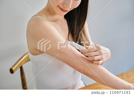 電気シェーバーで腕毛を剃る30代女性 110971191