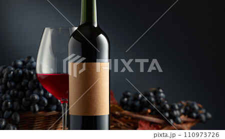 Bottle and glass of red wine with blue grapes. 110973726