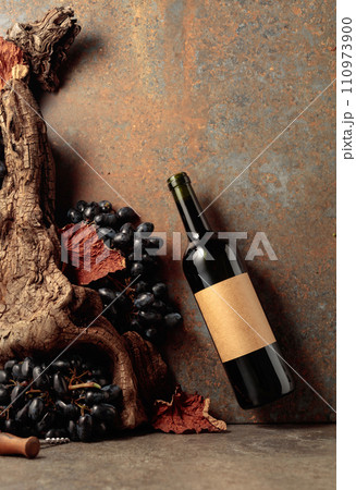 Bottle of red wine with blue grapes on a rusty background. Bottle of red wine with blue grapes on a rusty background. 110973900