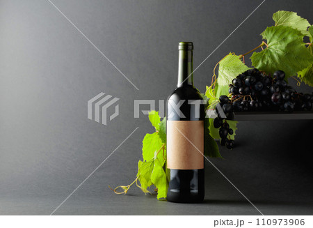 Bottle of red wine with blue grapes and vine branches. 110973906