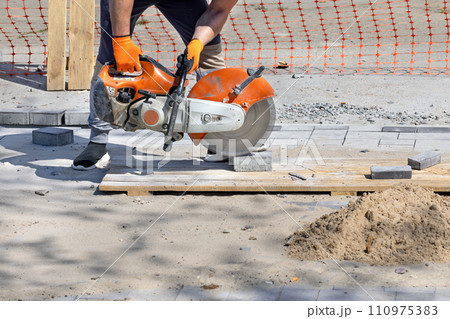 A worker cuts paving blocks at the workplace using a cutting saw and a diamond blade. 110975383
