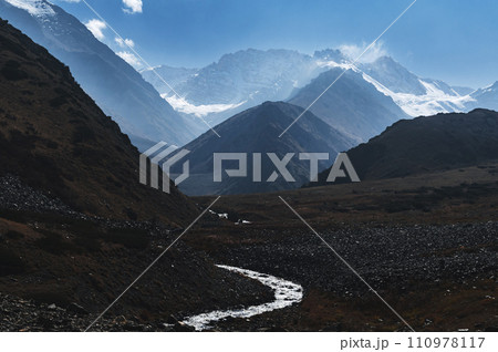 landscape with a river stream in mountains with peaks in the snow under blue sky in autumn landscape with a river stream in mountains with peaks in the snow under blue sky in autumn 110978117