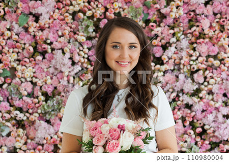 Joyful female model with rose flower in her hand standing on blooming floral blossom background 110980004