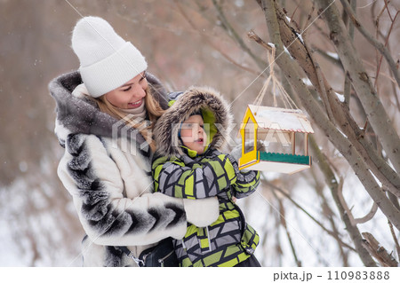 mother and son in a winter park feed birds using a feeder 110983888