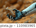 hand of a humanoid robot holds a mineral sample on a blurred deserted landscape 110983965