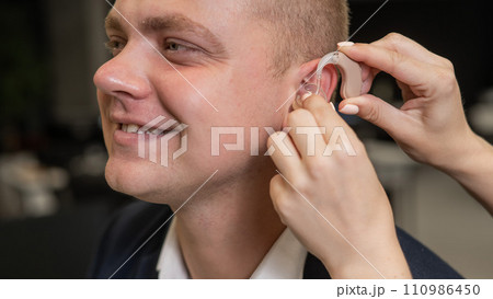 Woman putting hearing aid on Caucasian man. Woman putting hearing aid on Caucasian man. 110986450