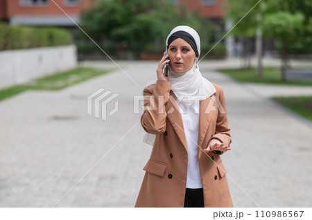 Young woman in hijab talking on smartphone outdoors.  110986567