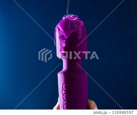 Intimate lubricant pours on a purple vibrator on a blue background. Copy space.  110986597