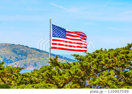 American flag against blue sky, trees, mountains American flag against blue sky, trees, mountains 110987599
