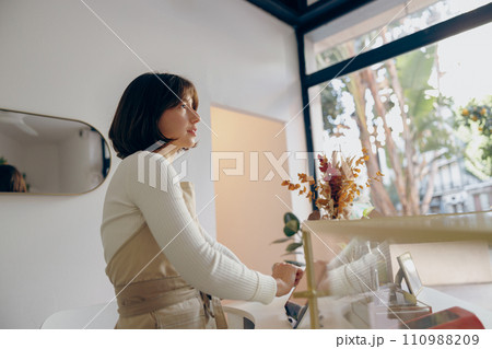 Female barista in arpon standing at the counter in coffee shop and takes orders from client Female barista in arpon standing at the counter in coffee shop and takes orders from client 110988209