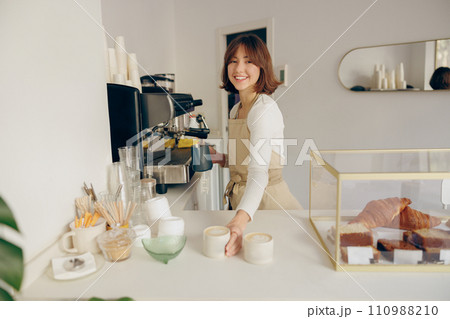 Beautiful female barista is looking at camera and smiling while working in coffee shop Beautiful female barista is looking at camera and smiling while working in coffee shop 110988210