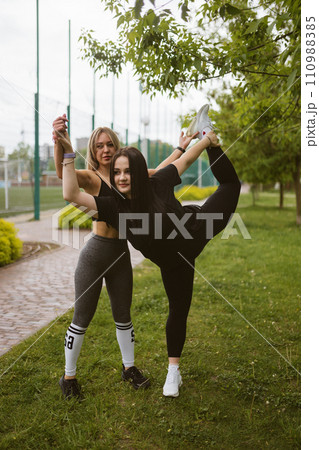 Fitness instructor supports woman lifting leg behind back 110988385