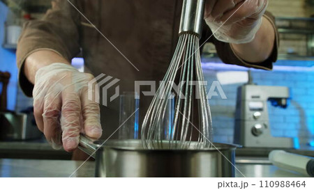 Carefully stirring mixture in saucepan culinarian turns off stove Carefully stirring mixture in saucepan culinarian turns off stove 110988464