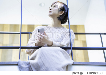 室内ブリッジに座ってスマホを使う女性 110989322