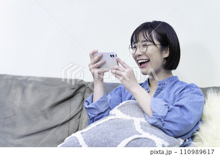 ソファーでスマホ動画を観る若い女性 110989617