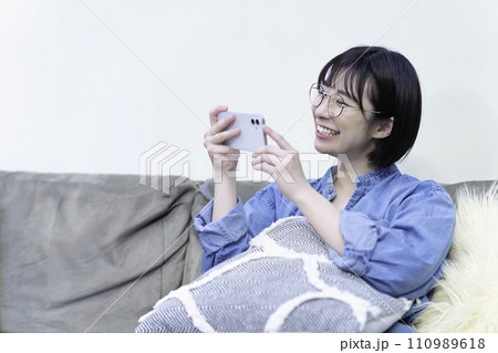 ソファーでスマホ動画を観る若い女性 110989618