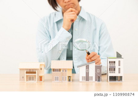 複数の住宅模型とルーペを持って悩むミドル女性 110990874