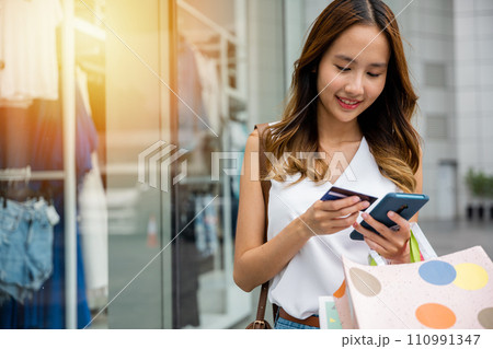 Consumer addiction in action ,young woman using her smartphone and credit card to make purchases while browsing an online store. Retail therapy at its most convenient 110991347