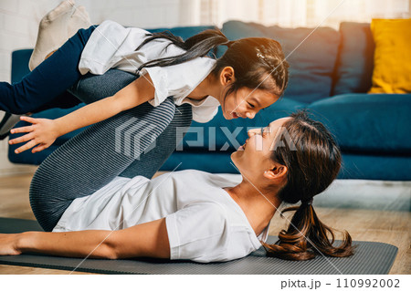 A mother holds her child in a playful family fitness pose imagining themselves 'flying' like airplanes during their Pilates and yoga routine promoting trust harmony and happiness. 110992002