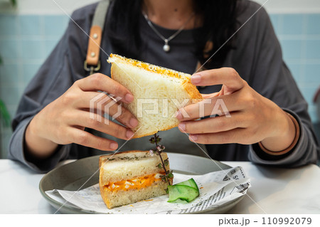Closeup of a woman holding and eating a sandwich with eggs and cheese and cucumber on a plate Closeup of a woman holding and eating a sandwich with eggs and cheese and cucumber on a plate 110992079