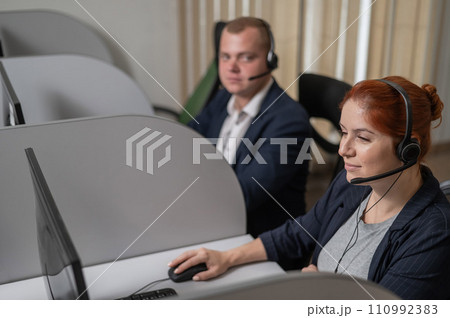 Two serious call center employees are talking with clients. Man and woman working with headsets in office.  110992383