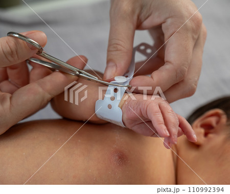 A woman cuts a tag from a newborn boy's hand with nail scissors. Close-up of hands. 110992394