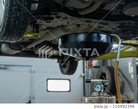 The process of changing the oil in a car engine. Draining old dark used oil from a car on a lift. The process of changing the oil in a car engine. Draining old dark used oil from a car on a lift. 110992396