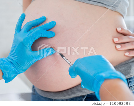 Doctor gives an injection in the stomach of a pregnant woman.  110992398
