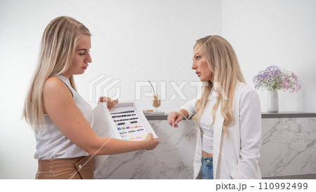 Eyelash extension master shows examples to a client. Woman choosing type of eyelash extension. Eyelash extension master shows examples to a client. Woman choosing type of eyelash extension. 110992499