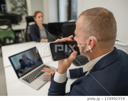 Caucasian man with a hearing aid talking on the phone on speakerphone.  110992559