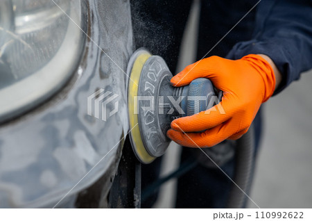 A mechanic sands the putty on a car body with a machine. Repair after an accident. A mechanic sands the putty on a car body with a machine. Repair after an accident. 110992622