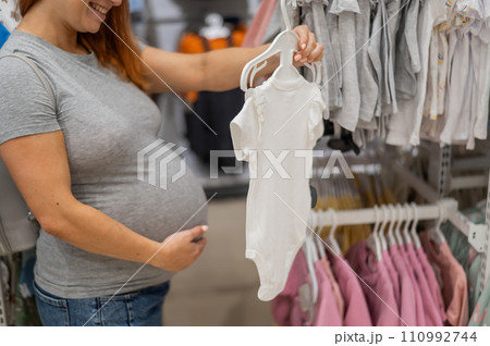 Caucasian pregnant woman chooses baby clothes in a store. Faceless expectant mother in the 3rd trimester.  110992744
