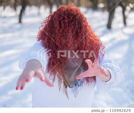 The plump-cheeked woman threw her red hair over her face and held out her arms like a zombie. Girl fooling around in the park in winter.  110992829