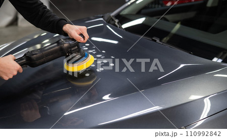 A mechanic polishes the surface of the hood of a gray car. A mechanic polishes the surface of the hood of a gray car. 110992842