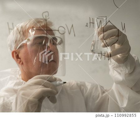 An elderly Caucasian male chemist in a protective suit writes on glass.  110992855