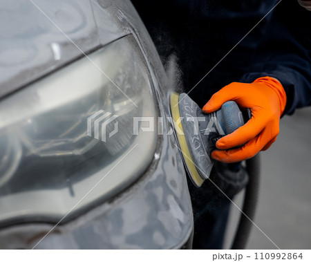 A mechanic sands the putty on a car body with a machine. Repair after an accident.  110992864