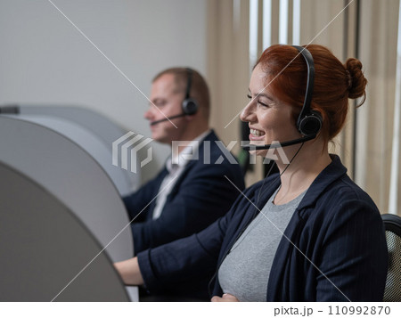 Two friendly call center employees answer customers by phone. Man and woman woman talking on a headset in the office. Two friendly call center employees answer customers by phone. Man and woman woman talking on a headset in the office. 110992870