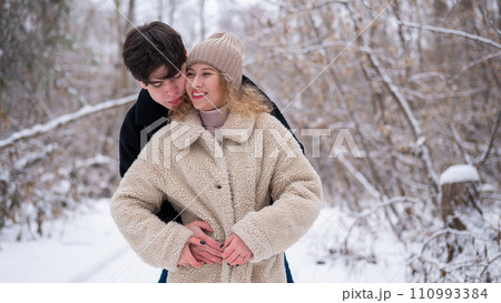 A young couple walks in the park in winter. Guy and girl hugging outdoors. 110993384